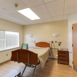 A well-lit and organized hospital patient room featuring a bed, window, and bedside furniture.