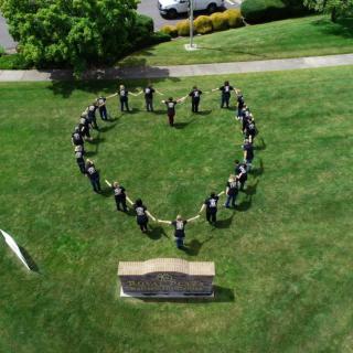 A group of people standing in a heart formation on a grassy field.