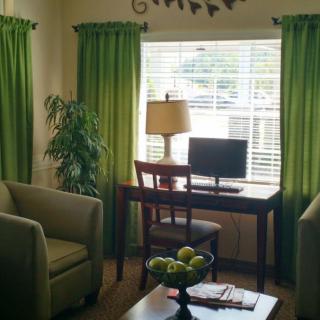 A cozy living room with a green color theme, featuring a desk with a computer and lamp by the window.