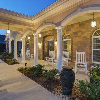 A welcoming porch with rocking chairs and elegant columns, beautifully lit in the evening.