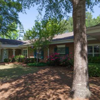 A suburban brick house with surrounding trees and well-maintained landscaping.