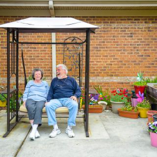 A couple sitting on a swing surrounded by colorful potted flowers in a garden area.