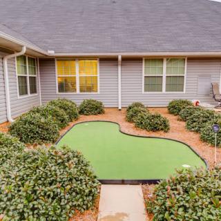 A residential courtyard with a mini golf putting green surrounded by shrubs.