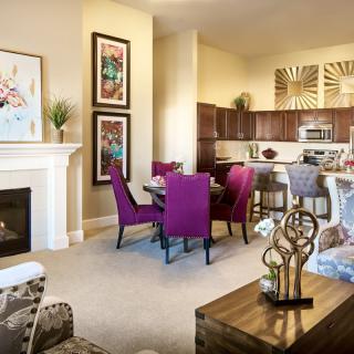 A modern open-plan living space featuring a cozy dining area with purple chairs, a stylish kitchen, and a welcoming fireplace.