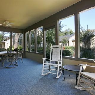 A bright sunroom with large windows, featuring rocking chairs and a dining table.