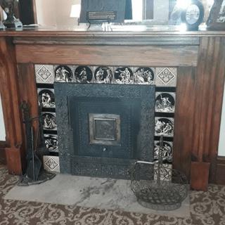 A vintage fireplace with a wooden mantle and ornate decorative tiles.