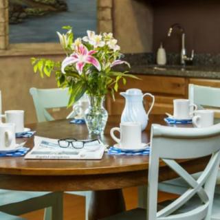 A cozy kitchen scene with a wooden dining table set for four, featuring a vase of fresh flowers and a newspaper.
