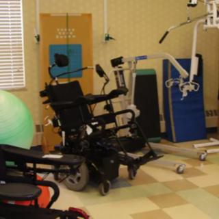A physical therapy room equipped with various rehabilitation tools and mobility aids, including wheelchairs and exercise equipment.