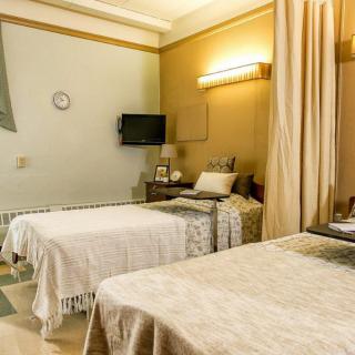 A hospital room with two beds, a television, and curtains separating the space.