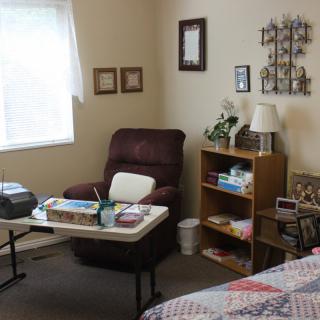 A cozy living room with a recliner, small bookshelf, and decorative items beside a window.
