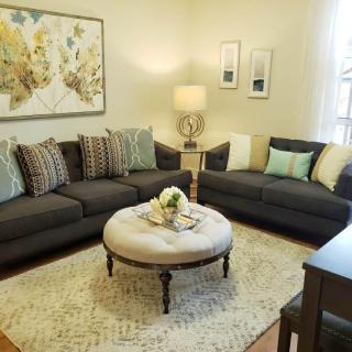 A cozy living room with two gray sofas, a round upholstered coffee table, decorative pillows, and artwork on the walls.