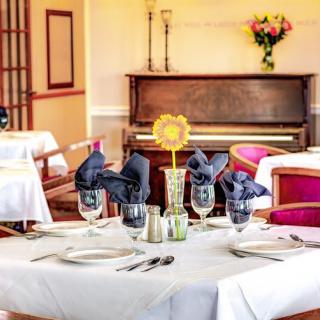 A beautifully set dining table in an elegant restaurant with a piano in the background.