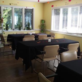 A cozy dining area with tables and chairs arranged neatly, featuring large windows and potted plants.