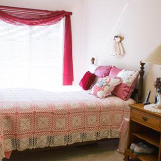 A cozy bedroom features a bed with pink decor and a nightstand with a lamp beside it.