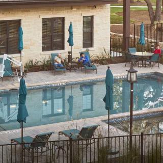 People relaxing by an outdoor swimming pool with deck chairs and umbrellas.