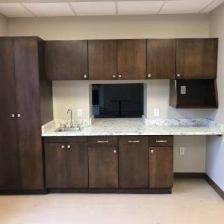 A modern kitchenette with brown cabinets and a countertop sink.