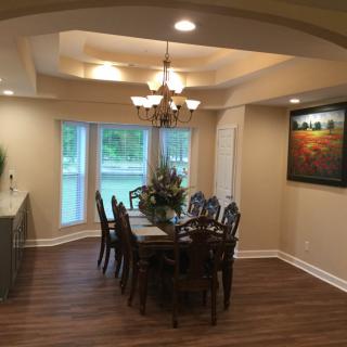 A beautifully designed dining room with a chandelier, wooden flooring, and elegant furniture, complemented by large windows and artwork.