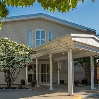 A welcoming entrance of a modern building surrounded by greenery under a clear blue sky.