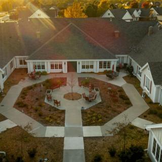 Aerial view of a symmetrical building with a central courtyard and surrounding gardens at sunset.