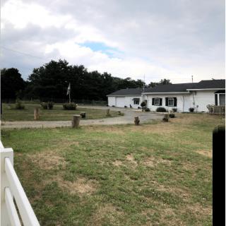 A view of a house with a large yard, surrounded by trees and under a cloudy sky.