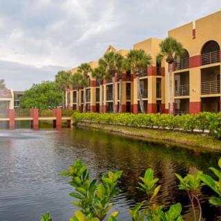 A scenic view of a building with palm trees reflected in the adjacent lake.