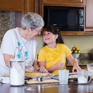 A grandmother and granddaughter smiling while baking together in the kitchen.