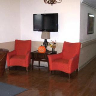 A cozy living room area with two red chairs, a table with a lamp and pumpkin, and a wall-mounted television.