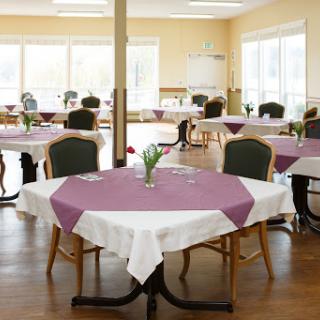 A spacious dining area featuring elegantly set tables with purple tablecloths and floral centerpieces.