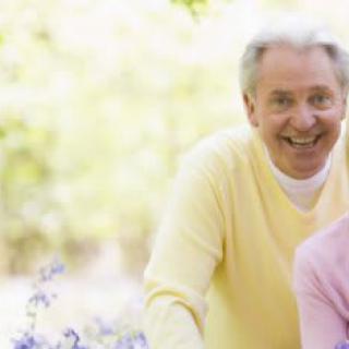 An elderly man smiling outdoors in a natural setting.