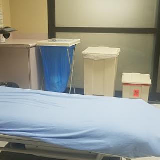 A hospital room featuring a medical bed covered with a blue sheet and waste disposal bins.