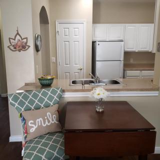 A cozy kitchen and dining area with modern touches, featuring a chair with a 'smile' pillow, a small table, and a flower vase.