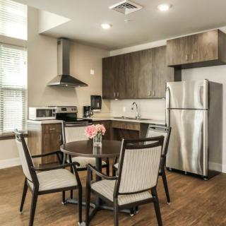 A modern kitchen and dining area with stainless steel appliances, wooden cabinets, and a round table with chairs on a hardwood floor.
