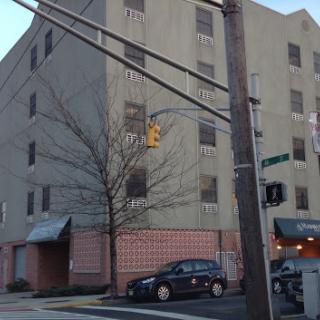 A view of a multi-story building on a city street, featuring parked cars and traffic signals.