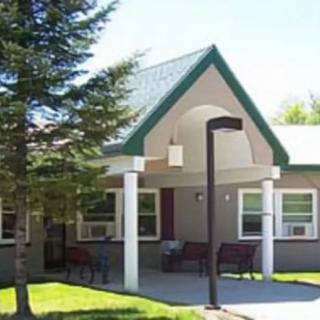 A small residential building with a green roof and trees in the front yard.