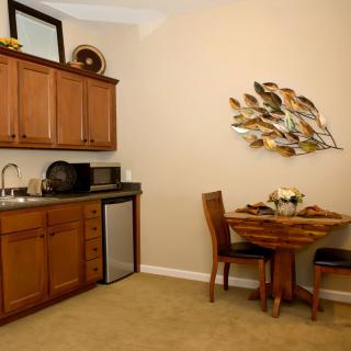 A compact kitchen and dining area with wooden cabinets, a small table and chairs, and decorative wall art.