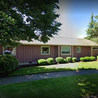 A single-story house with a well-maintained lawn and shrubbery under a clear blue sky.
