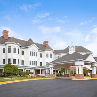 A large white residential building with a covered entrance under a partly cloudy sky.