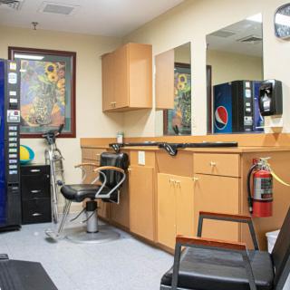 A cozy barber shop interior featuring a styling chair, mirrors, cabinets, and a vending machine.