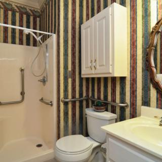 A small bathroom featuring a shower, toilet, sink, and a wall-mounted cabinet with striped wallpaper.