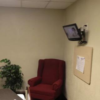 A small office waiting area with a red armchair, wall-mounted TV, a plant, and a notice board.