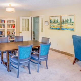 A well-lit conference room with a large table and blue chairs, featuring bookshelves and artwork on the walls.
