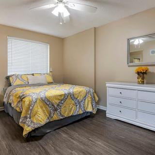 Cozy bedroom with a yellow-patterned bedspread, white dresser, and ceiling fan.