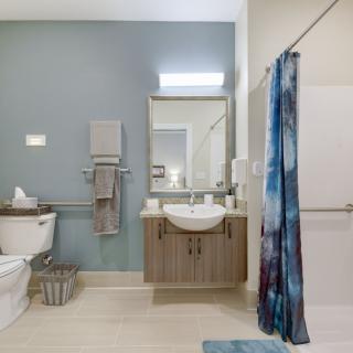 A modern bathroom with a central mirror and sink, featuring a toilet on the left and a shower area with a blue shower curtain.