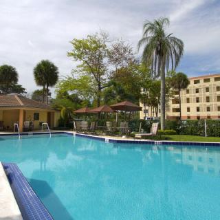 A serene outdoor swimming pool surrounded by tropical palm trees and resort buildings.