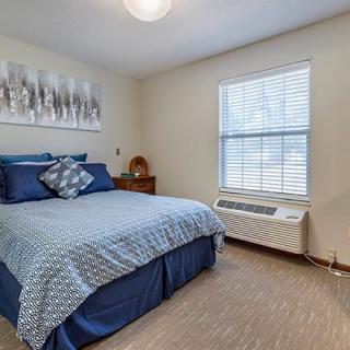 A cozy bedroom with a neatly made bed, artwork on the wall, and a window allowing natural light.