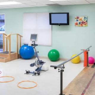 A physical therapy room equipped with exercise balls, a stationary bike, parallel bars, and other rehabilitation tools.