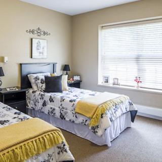 A cozy bedroom with twin beds featuring floral bedding and sunny natural light streaming through the window.