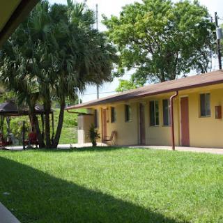 A sunny residential area featuring a yellow building surrounded by lush green grass and palm trees.