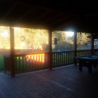 A peaceful view of a covered deck overlooking a fenced yard bathed in sunlight.