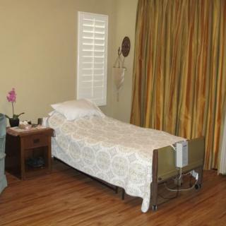 A simple bedroom with a hospital bed, wooden floor, and curtains.